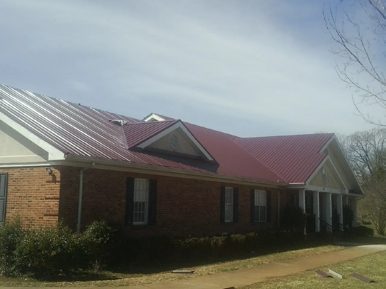 Red metal roof with gabled entries on a long brick building, from a Hail Damage Roof Repair job in Monrovia
