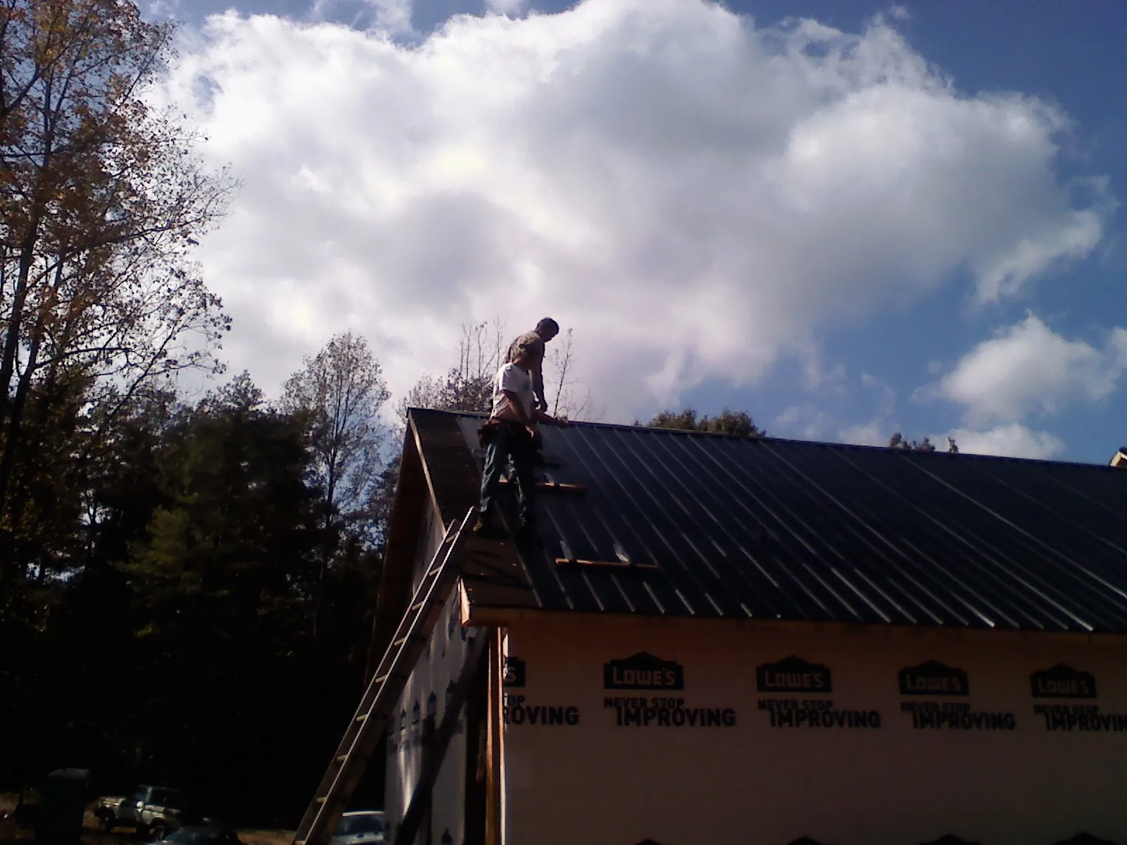 Roofer fastening dark metal panels high against a cloudy sky, from a Roof Inspection job in Monrovia